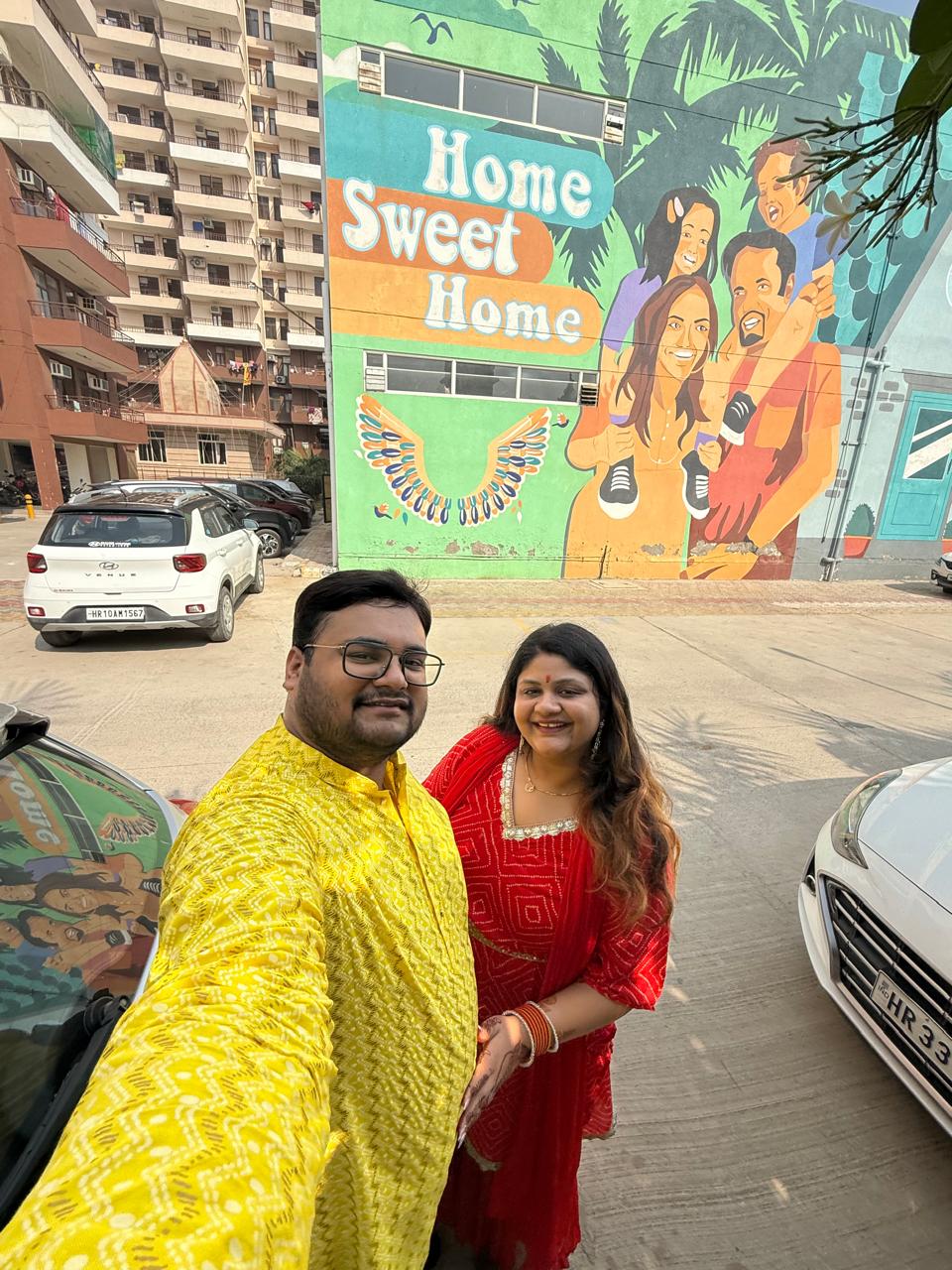 Salil and Eesha taking a festive selfie near a Home Sweet Home mural